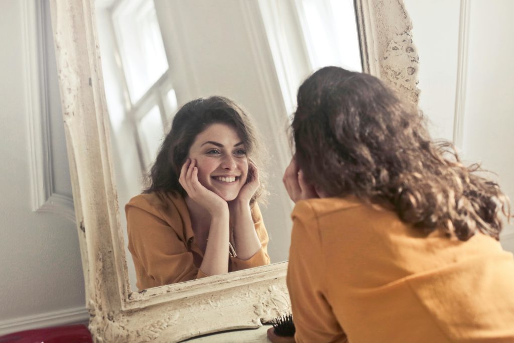 Una chica sonriendo y mirándose al espejo para una artículo de Vivir en Astrológico.